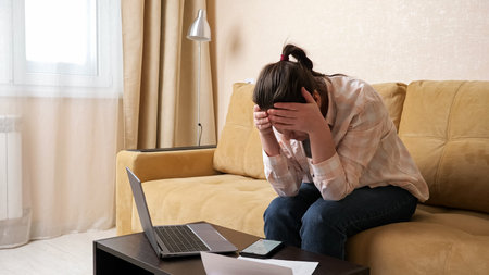 Upset woman tries to calculate high payments on modern mobile phone and holds head in frustration...