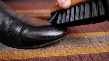 Close-up of a shoe brush rubs a black leather boot.の写真素材