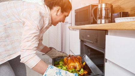 woman pulls ready food out of the oven, chicken with vegetables, home cooking