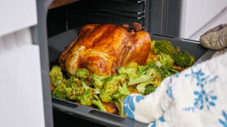 Lady take out crispy chicken with vegetables on a baking sheet from the ovenの写真素材