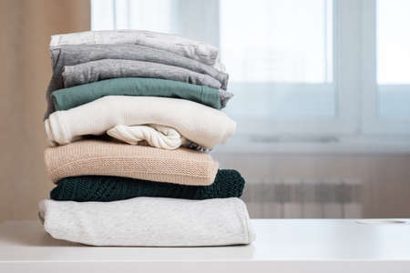 stack of sweater on white table against large window in brightly lit room closeupの写真素材