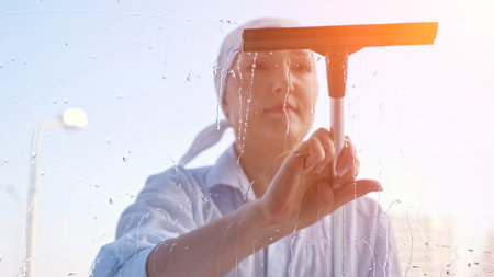 Young woman washing the window with a scraper, sunlightの写真素材