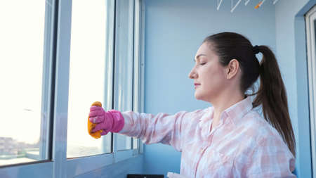 Young woman in gloves with spray and rag washes the window.の写真素材