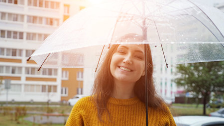 happy young woman stands under transparent umbrella in the rain, sunlight