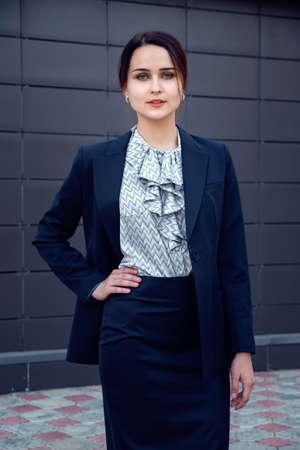 young woman in a suit stands and looks at camera posing on the street near the building.の写真素材