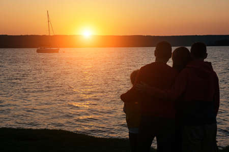 Silhouette of children with parents hugs at sunset, summertimeの写真素材