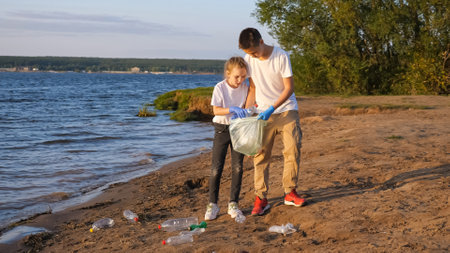 young girl with brother collecting trash in bags near the coast at sunsetの写真素材