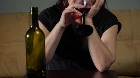 unrecognizable tipsy woman with stressed face expression drinks wine sitting on soft sofa in living room.の写真素材