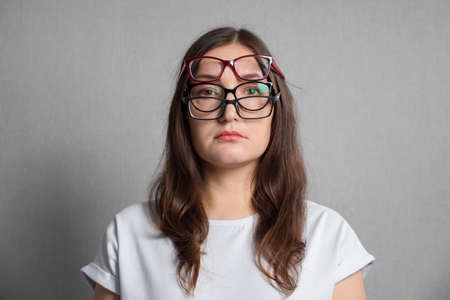 Young dark-haired woman with poor eyesight dressed in white t-shirt puts on several pairs of glasses sadly to improve low vision closeupの写真素材