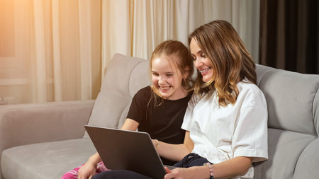 Happy mother and teen daughter in black and white t-shirts watch funny photos on laptop laughing on...