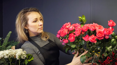 Professional florist in black apron takes fresh pink roses from glass vase to make elegant romantic...