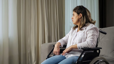 Sad disabled woman with organic damage of central nervous system sits in wheelchair looking out of...