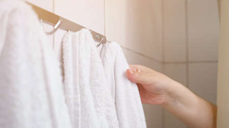 Female hand pulls back bath curtain and removes towel from hook. Woman takes terry towel after taking shower during morning routine, sunlightの写真素材
