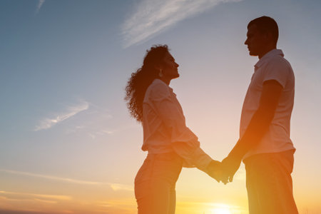 Loving couple looks at each other against sky with sunset. Partners man and woman hold hands gently enjoying special moments together on natureの写真素材