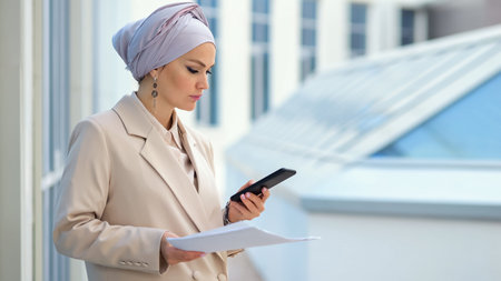 Muslim businesswoman in silver hijab looks through signed documents waiting for call from business partner. Entrepreneur reads with serious expressionの写真素材