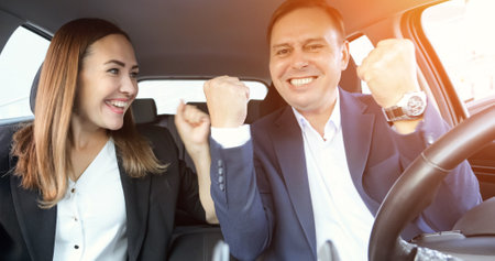 Glad office worker in suit sits in automobile and rejoices with colleague. Man and woman enjoy victory celebrating good deal and concluding agreement, sunlightの写真素材