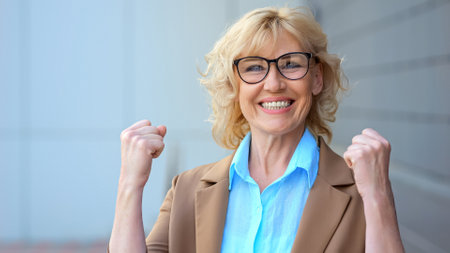 Joyful businesswoman rejoices from good news regarding work standing on blurred background of business office. Female worker happy from received working tidingsの写真素材