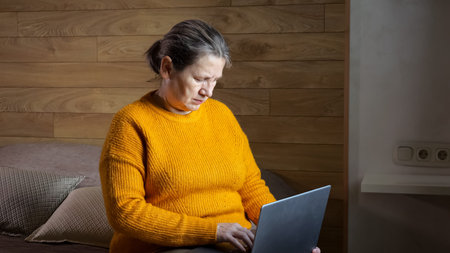 Mature woman searches information on laptop. Short-haired freelancer types information on modern...