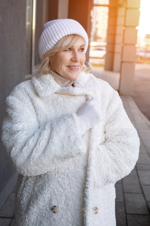 Stylish senior woman wearing a white coat and winter hat enjoying a sunny winter day in the cityの写真素材