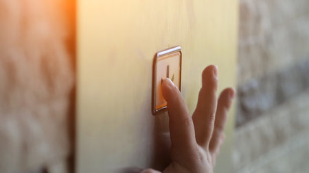 Child hand presses on button with arrow in modern lift. Button glows softly with red colour under touch signaling movement of elevatorの写真素材