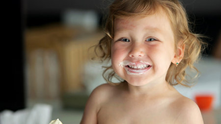 Cheerful preschooler girl enjoys ice cream with big smile. Face of smiling child becomes delightfully messy capturing innocence and pure happinessの写真素材