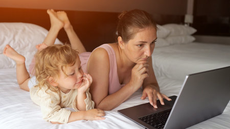 Businesswoman working remotely on vacation, balancing work and family time with her child in a hotel roomの写真素材