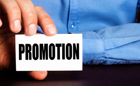 PROMOTION is written on a white business card in a man's hand. Advertising conceptの写真素材
