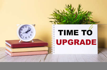 TIME TO UPGRADE written in a notebook near a white alarm clockの写真素材