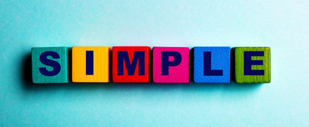 The word SIMPLE is written on multicolored bright wooden cubes on a light blue background