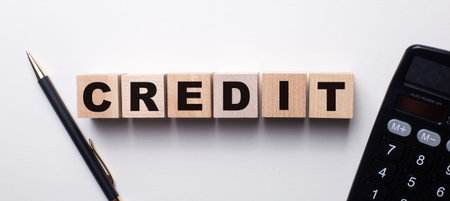 The word CREDIT is written on wooden cubes on a light table near a calculator and pens. Financial...