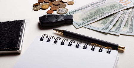 The car key, calculator, money, pen and blank notepad lie on a white table. Business Concept Copy...