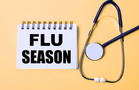 On a beige background, a stethoscope and a white notepad with the inscription FLU SEASON Medical conceptの写真素材