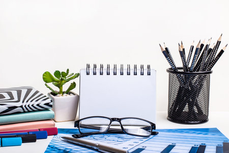On the desktop there are pencils in a stand, glasses, notebooks, a pen, a plant in a pot. Workplace...