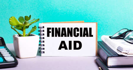 FINANCIAL AID is written on a white card next to a flower in a pot, a diary and a calculator on the desktop. Financial conceptの写真素材