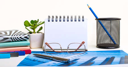 On the desktop there are pencil in a stand, glasses, notebooks, a pen, a plant in a pot. Workplace close-up. Copy space. Business conceptの写真素材