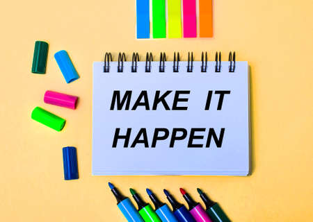 On a beige background, a notebook with the inscription MAKE IT HAPPEN, bright felt-tip pens and stickers.の写真素材