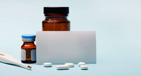 On a light blue background - pills, an electronic thermometer, medicine bottles and a white business card. Medical conceptの写真素材