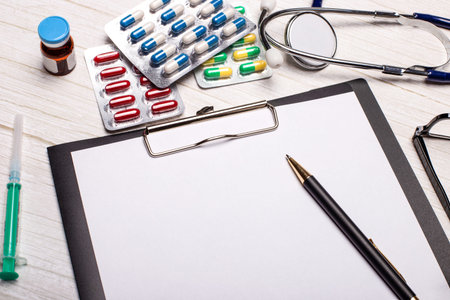 On the table are a stethoscope, bright pills, a syringe and a notebook with a pen. Copy space....