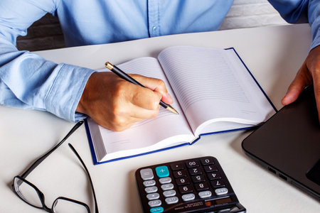 A businessman in a blue shirt sits at his desk and writes in a notebookの写真素材