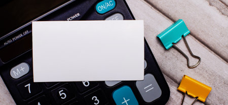 Stationery concept. Calculator, multi-colored paper clips and a white blank card on a light wooden table. Stationery and calculator.の写真素材