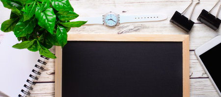 On a light wooden background there is a black board for inscriptions, a clock, a telephone, a notebook. Copy space.の写真素材