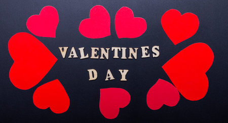 Valentines Day is written on a black background near red hearts. Romantic concept.