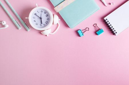 Stationary concept, top view Flat Lay Photo of pencils, paper clips, alarm clock, notepads, in white and blue on pink background with copy space.の写真素材