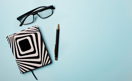 Notepad, pen and glasses on a light blue background. Copy space