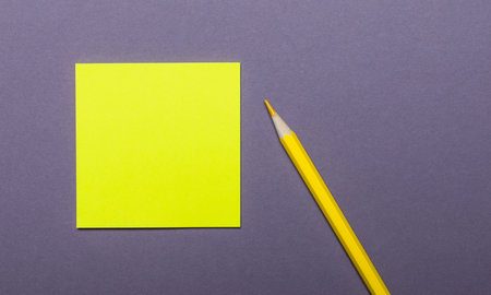 On a gray background, a bright yellow pencil and a yellow sticker for inscriptions or drawingの写真素材