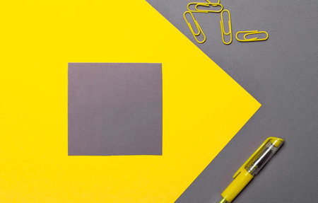 Gray sticker with space to insert text or illustrations on a yellow background. Nearby on a gray background are yellow paper clips and a yellow pen. Copy spaceの写真素材
