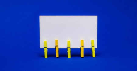 On bright blue background on yellow clothespins white blank card with copy space