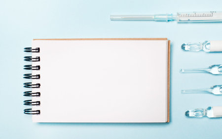 On a light blue background ampoules, a syringe and a blank notebook. Top view with copy space....