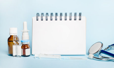 On a light background, a syringe, a stethoscope, vials of medicine, an ampoule and a blank white notepad to insert text. Medical conceptの写真素材