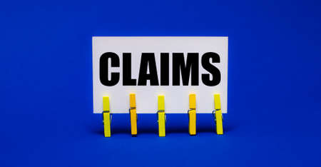 On a bright blue background on yellow clothespins, a white card with the text CLAIMSの写真素材